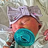 baby, bedding, blanket, bow, closed_eyes, closeup, clothing, cozy, face, hand, headband, hospital, indoors, infant, newborn, pacifier, portrait, sleeping, swaddled, textile
