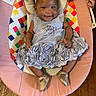 baby, infant, dress, flower_headband, smile, baby_seat, plush_toy, sun_toy, cloud_toy, colorful, wooden_floor, silver_shoes, happy, cute, indoors, child, person, sitting, headband, toddler