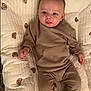 baby, infant, child, quilt, cushion, bear_pattern, brown_outfit, clothing, smile, face, head, hand, footwear_absent, indoors, soft_lighting, portrait, lying_down, cute, comfort, baby_garment