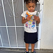 Nene joined the competition — help win amazing prizes! child, toy, dinosaur, elephant, tshirt, skirt, slippers, standing, concrete, gate, metal, emotion, cartoon, outdoor, person, hair, play, young, casual, curly_hair
