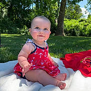 Iris is registered to the contest to win money with this photo: baby, child, outdoor, grass, tree, blanket, dress, red, anchor_pattern, smiling, sitting, cute, sunlight, nature, playtime, barefoot, happy, person, infant, summer