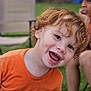 child, toddler, red_hair, orange_shirt, smiling, outdoor, grass, backyard, happy, face, person, young, cheerful, curly_hair, playing, fun, sitting, chair, blurred_background, summer