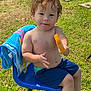 toddler, child, outdoor, grass, chair, popsicle, blue, towel, summer, curly_hair, bare_chest, shorts, food, snack, sunlight, playful, happy, face, person, nature