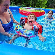 Zayden is registered to the contest to win money with this photo: child, toddler, woman, swimming_pool, floaties, inflatable_pool, water, smiling, laughing, outdoor, summer, trees, greenery, fun, family, recreation, play, people, toy, pool_toy