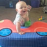 baby, car_toy, carpet, child, colorful, crawling, cute, furniture, happy, indoor, infant, living_room, person, play, playtime, plush_toy, smiling, storage_bin, table, toy