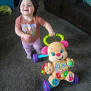 Ivana joined the competition — help win amazing prizes! toddler, child, toy, walker, indoor, carpet, living_room, hat, smile, colorful, purple, green, pink, brown_couch, plastic_toy, person, play, happy, blur, floor