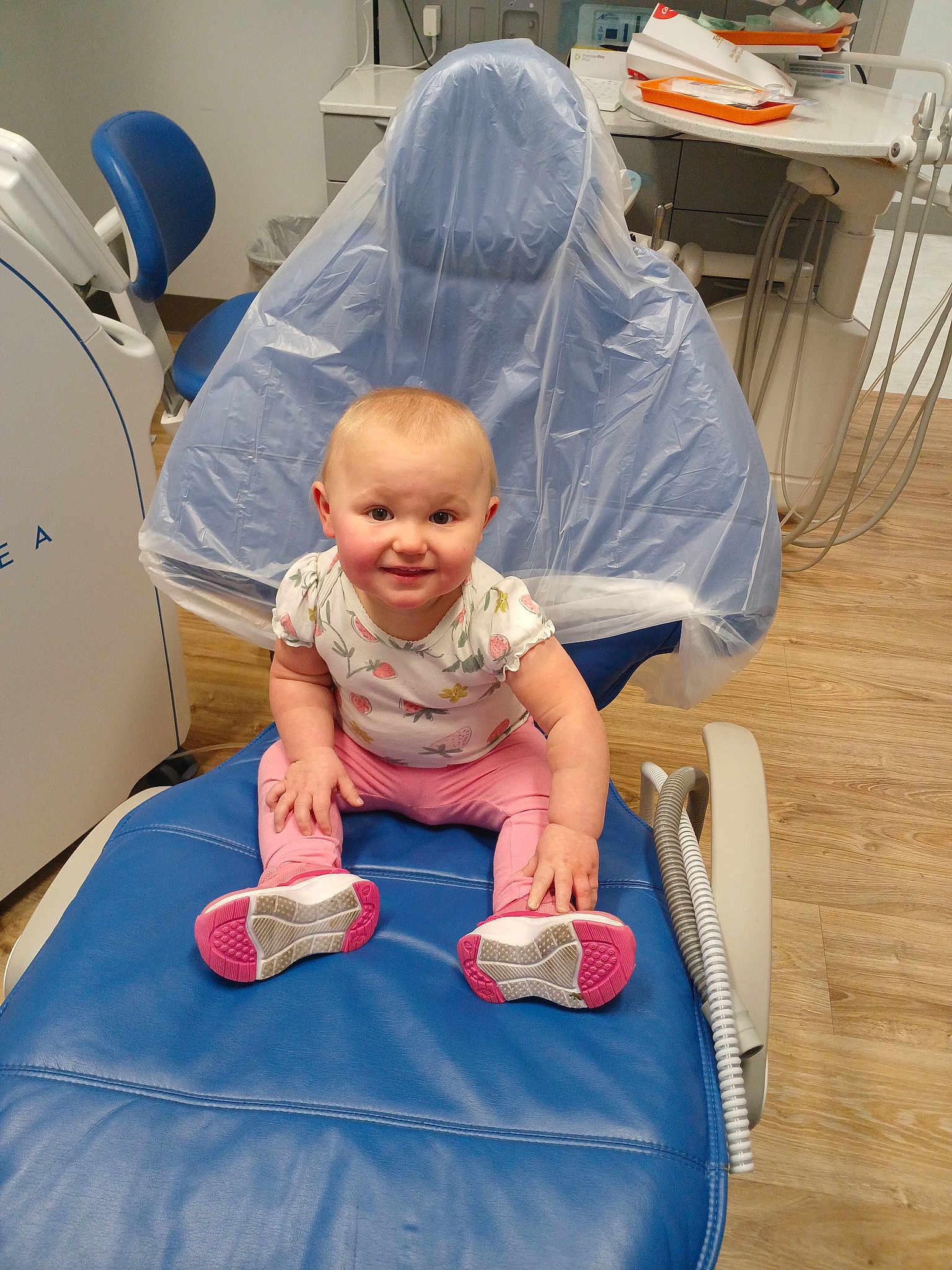 Ivana joined the competition — help win amazing prizes! baby, child, dental_chair, dentist_office, floor, pink_clothing, blue_chair, smile, happy, person, footwear, shoes, medical_equipment, room, wood_floor, plastic_cover, cabinet, toy, indoor, curly_hair