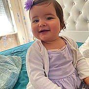 Giulia participe au concours pour gagner de l'argent avec cette photo : baby, child, smiling, girl, flower_clip, purple_dress, white_cardigan, bed, pillow, teal_bedspread, indoor, portrait, happy, cute, headboard, wallpaper, window, natural_light, person, infant