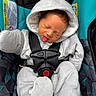 baby, infant, child, car_seat, onesie, hood, tongue_out, straps, cozy, sleepy, cute, seatbelt, patterned, fabric, small_person, portrait, indoors, soft_texture, wrapped, secure