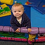 toddler, child, indoor, play_area, colorful, padded_barrier, smiling, curly_hair, blue_sweater, soft_toys, foam_mats, carpet, baby, cute, play, happy, young_child, hands, portrait, crawling