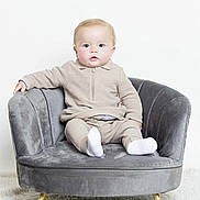 Hudson is registered to the contest to win money with this photo: baby, child, infant, sitting, chair, velvet, grey, beige_clothing, white_socks, carpet, indoor, portrait, cute, young_child, furniture, soft_texture, curious, studio, minimalist, comfortable