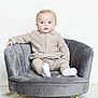 baby, child, infant, sitting, chair, velvet, grey, beige_clothing, white_socks, carpet, indoor, portrait, cute, young_child, furniture, soft_texture, curious, studio, minimalist, comfortable