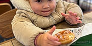 Tallulah joined the competition — help win amazing prizes! blurred_background, cafe, child, clothing, coat, cute, donut, expression, face, food, glazed_donut, hand, hood, indoor, jacket, person, sitting, table, toddler, wood