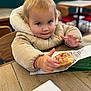 blurred_background, cafe, child, clothing, coat, cute, donut, expression, face, food, glazed_donut, hand, hood, indoor, jacket, person, sitting, table, toddler, wood