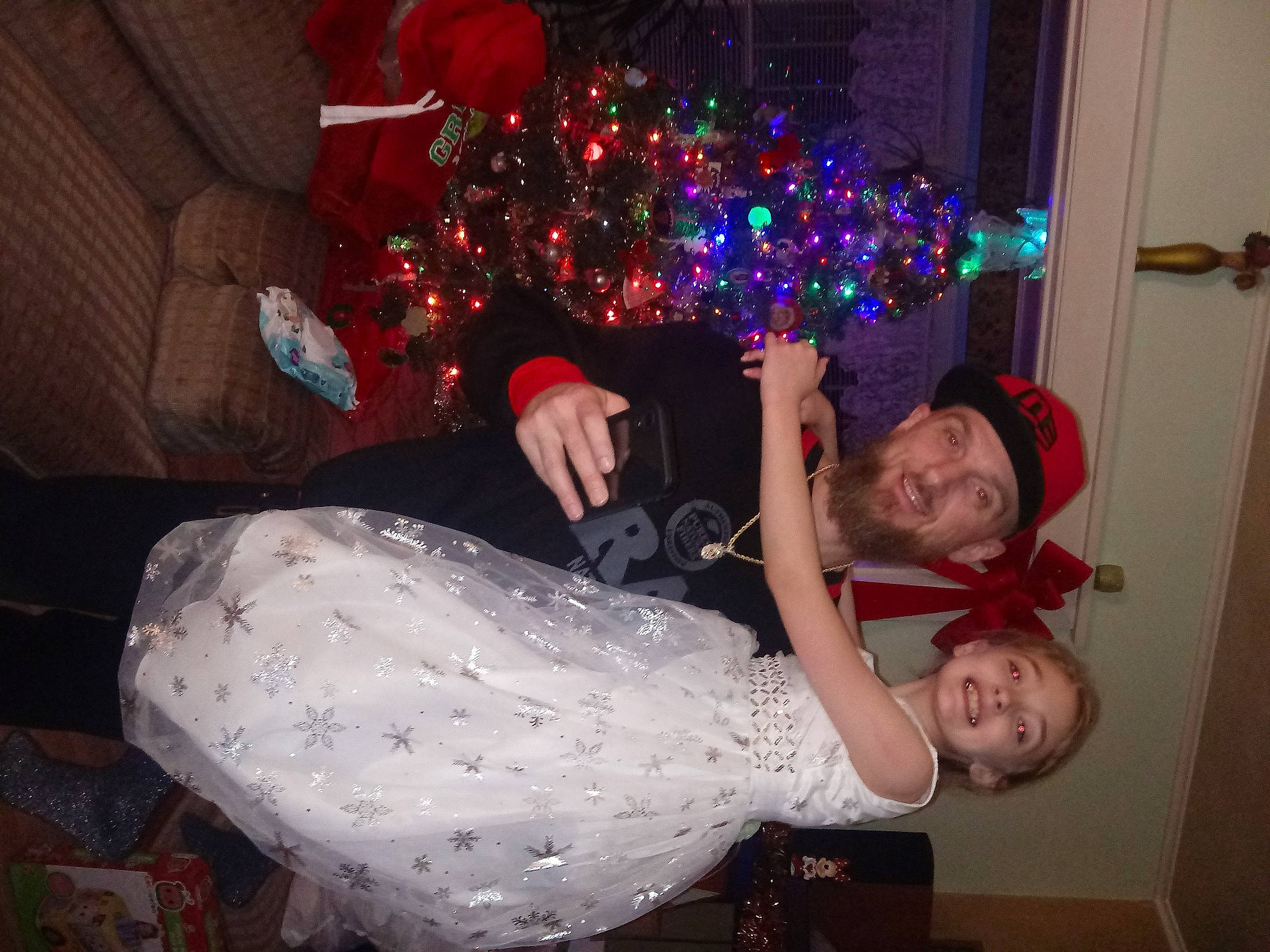 Emma is registered to the contest to win money with this photo: christmas, christmas_decoration, christmas_eve, christmas_ornament, christmas_tree, door, event, fun, happy, headwear, holiday, holiday_ornament, joy, lap, ornament, party, party_supply, person, room, smile