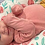 baby, infant, pink_clothing, smile, face, blue_eyes, blanket, floral_pattern, soft_texture, lying_down, cute, child, cozy, sleepwear, portrait, closeup, skin, resting, indoors, comfort