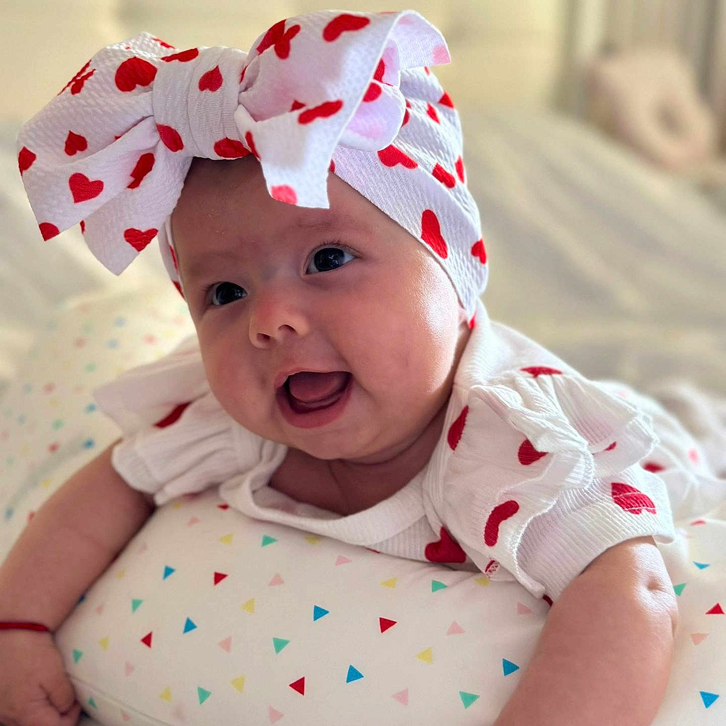 Lia Mihailuta a rejoint le concours — aidez-le/la à gagner de superbes lots ! baby, bedroom, child, chubby_cheeks, closeup, cute, happy, headband, indoor, infant, infant_girl, lying_down, pillow, portrait, red_hearts, skin, smiling, soft_light, triangle_pattern, white_clothing
