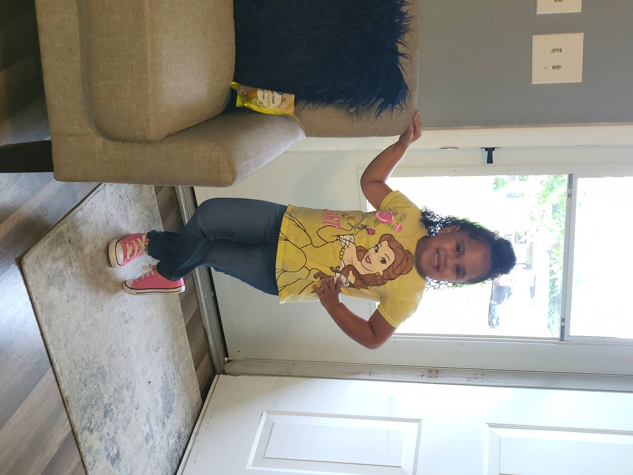 Brylee is registered to the contest to win money with this photo: balance, child, elbow, flooring, fun, human_leg, joy, knee, leg, person, room, smile, t_shirt, thigh, toddler, window, wood, wrist
