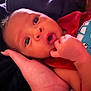 Tyhir is registered to the contest to win money with this photo: baby, infant, hand, face, eyes, clothing, red_shirt, blue_graphic, skin, expression, curious, portrait, closeup, child, person, newborn, resting, background, soft_light, indoor