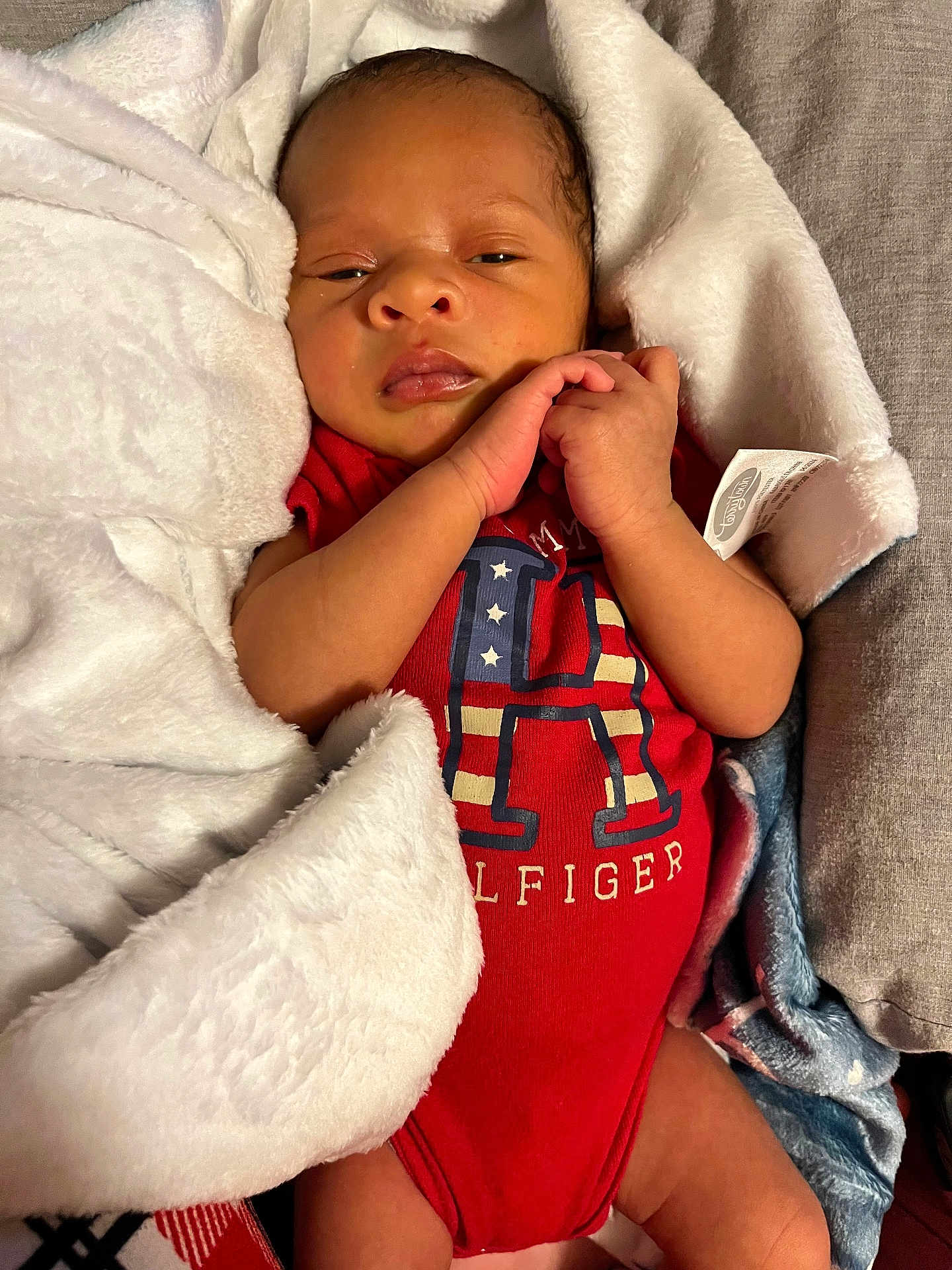 Tyhir is registered to the contest to win money with this photo: newborn, baby, infant, blanket, red_onesie, clothing, face, hands, cozy, sleepy, cute, portrait, indoors, resting, soft_texture, human, skin, wrapped, lying_down, toddler