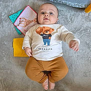 élio a rejoint le concours — aidez-le/la à gagner de superbes lots ! baby, infant, carpet, clothing, teddy_bear, basketball, toy, blanket, floor, person, child, indoor, cute, looking_up, socks, pants, long_sleeves, playtime, soft_surface, colorful