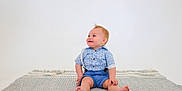 Pablo is registered to the contest to win money with this photo: baby, child, smiling, blue_clothing, suspenders, sitting, barefoot, rug, indoor, portrait, happy, cute, infant, one_person, studio, casual, light_background, short_hair, looking_away, small_person