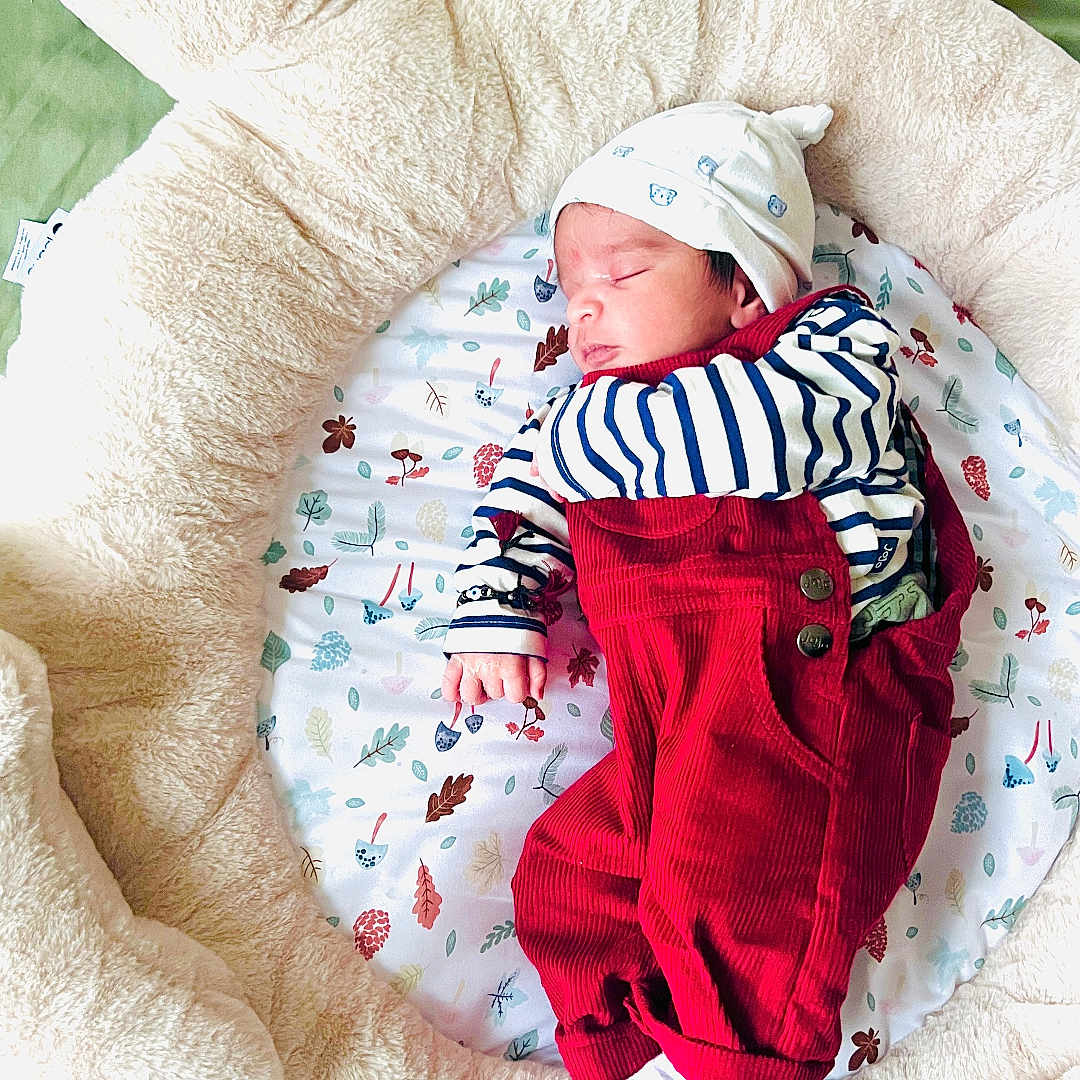 Sambhrit joined the competition — help win amazing prizes! baby, bed, child, comfort, cozy, cushion, cute, green_blanket, hat, indoors, infant, leaf_pattern, newborn, plush_toy, red_overalls, resting, sleeping, soft, striped_shirt, teddy_bear