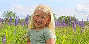 Elizabeth joined the competition — help win amazing prizes! child, girl, smiling, blonde_hair, flower_field, purple_flowers, greenery, outdoor, nature, sky, clouds, summer, casual_clothing, short_sleeve, happy, portrait, grass, sunlight, playful, scenic