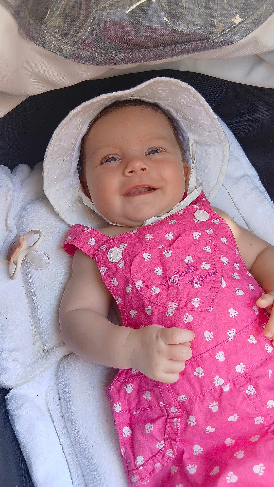 Iria a rejoint le concours — aidez-le/la à gagner de superbes lots ! baby, smiling, white_hat, pink_overall, minnie_mouse, pacifier, towel, infant, cute, child, portrait, clothing, hand, face, happy, lying_down, closeup, outdoor, baby_girl, soft_light