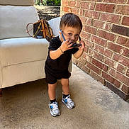 Ean is registered to the contest to win money with this photo: toddler, child, sunglasses, black_clothing, sneakers, concrete_floor, brick_wall, white_chair, handbag, outdoor, daylight, standing, looking_at_camera, cute, bracelet, casual, portrait, person, fashion, accessory