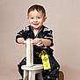 Ean is registered to the contest to win money with this photo: toddler, child, smiling, ride_on_toy, wooden_toy, black_clothing, pants, shoes, studio_photo, beige_background, happy, face, hands, short_hair, sitting, cute, fashion, portrait, indoor, play