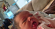 Serenity is registered to the contest to win money with this photo: baby, blanket, child, clothing, couch, cozy, cute, expression, face, hand, home, indoors, infant, living_room, newborn, person, portrait, sleepy, soft_lighting, tongue_out