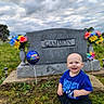 Zaidyn is registered to the contest to win money with this photo: baby, balloon, birthday, blue_shirt, cemetery, child, cloudy_sky, flowers, grass, gravestone, greenery, happy, headstone, memorial, nature, outdoor, pinwheel, portrait, sitting, smiling