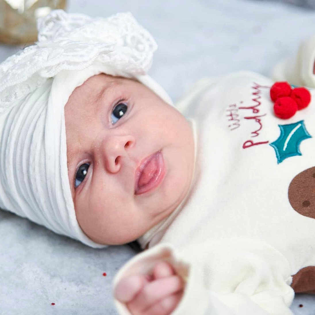 Azalea-Jae joined the competition — help win amazing prizes! adorable, baby, bow, celebration, child, closeup, cute, expression, face, festive_outfit, headwrap, holiday, indoors, infant, lying_down, newborn, portrait, soft_texture, tongue_out, white_clothing