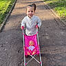 Mya participe au concours pour gagner de l'argent avec cette photo : child, doll, stroller, pink, park, pathway, grass, trees, outdoor, sunny, casual_clothing, smiling, play, toy, person, young_child, daylight, nature, recreation, happy