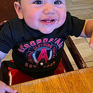 Micah is registered to the contest to win money with this photo: toddler, child, smiling, happy, table, wooden_table, black_shirt, red_pants, indoor, person, face, short_hair, clothing, sitting, restaurant, high_chair, bright, cute, young, casual