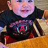 toddler, child, smiling, happy, table, wooden_table, black_shirt, red_pants, indoor, person, face, short_hair, clothing, sitting, restaurant, high_chair, bright, cute, young, casual