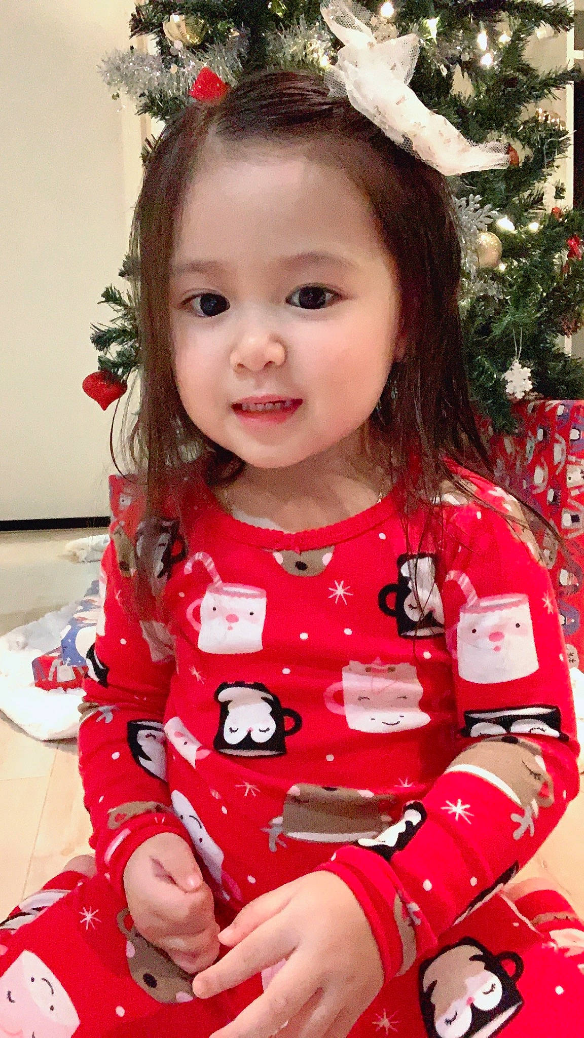 Yumi is registered to the contest to win money with this photo: baby_toddler_clothing, child, christmas_tree, dress, eye, face, facial_expression, hairstyle, happy, lip, outerwear, pattern, person, pink, red, skin, sleeve, smile, standing, toddler