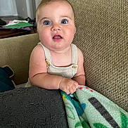 Gianna is registered to the contest to win money with this photo: baby, child, infant, blue_eyes, blanket, couch, indoor, person, portrait, cute, curious, chubby_cheeks, knit_clothing, texture, comfort, home, seated, hand, expression, furniture