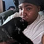affection, black_cat, black_fur, bonnet, cat, close_up, comfortable, couch, cozy, facial_expression, feline, home, indoor, nose_ring, person, pet, relaxed, snuggling, whiskers, white_shirt