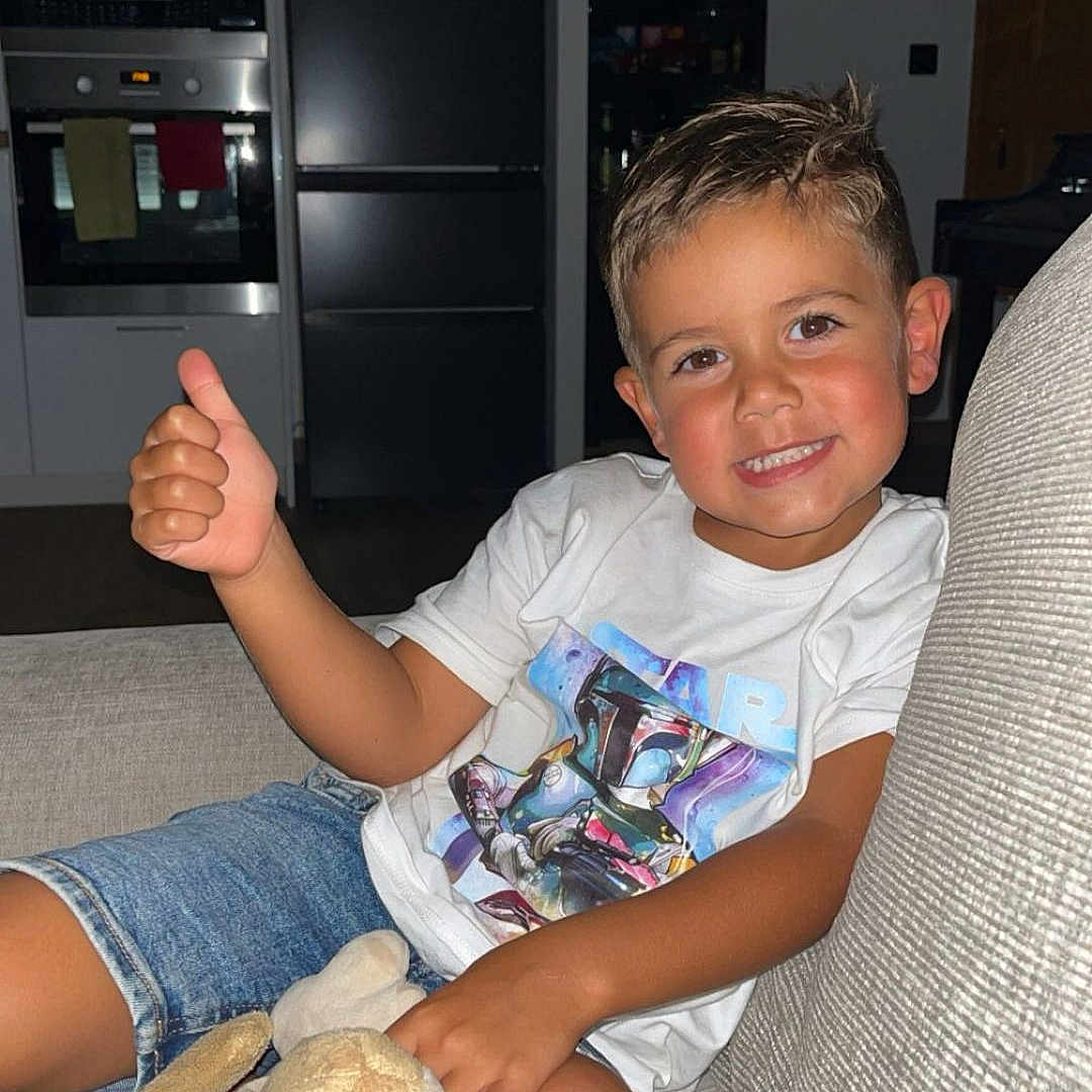 Noah participe au concours pour gagner de l'argent avec cette photo : boy, cabinet, casual_clothing, child, couch, denim_shorts, happy, home, indoor, kitchen, oven, plant, plush_toys, portrait, refrigerator, relaxed, smiling, star_wars_tshirt, stuffed_animals, thumbs_up
