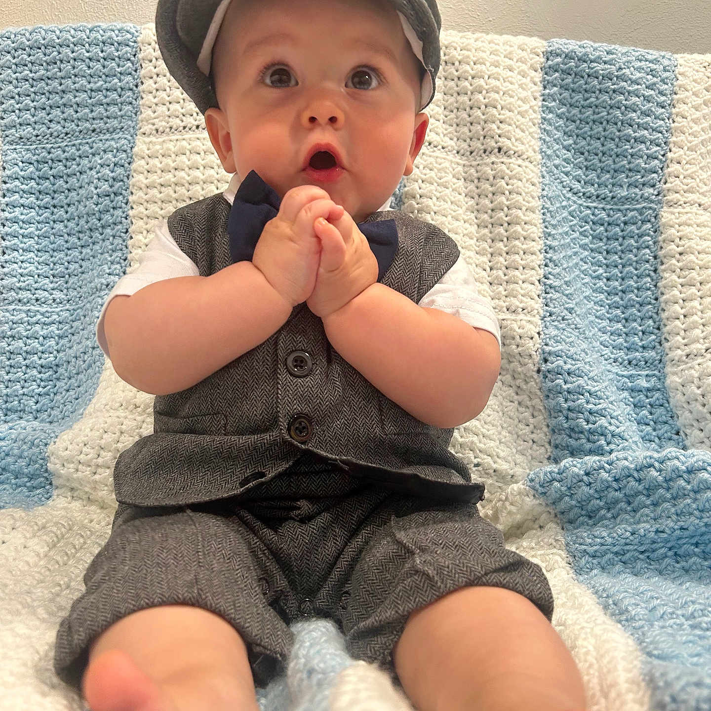 Simon is registered to the contest to win money with this photo: baby, child, infant, clothing, vest, shorts, cap, bowtie, knitted_blanket, sitting, cute, hands_clasped, wide_eyes, indoors, portrait, soft_lighting, expression, foot, couch, home