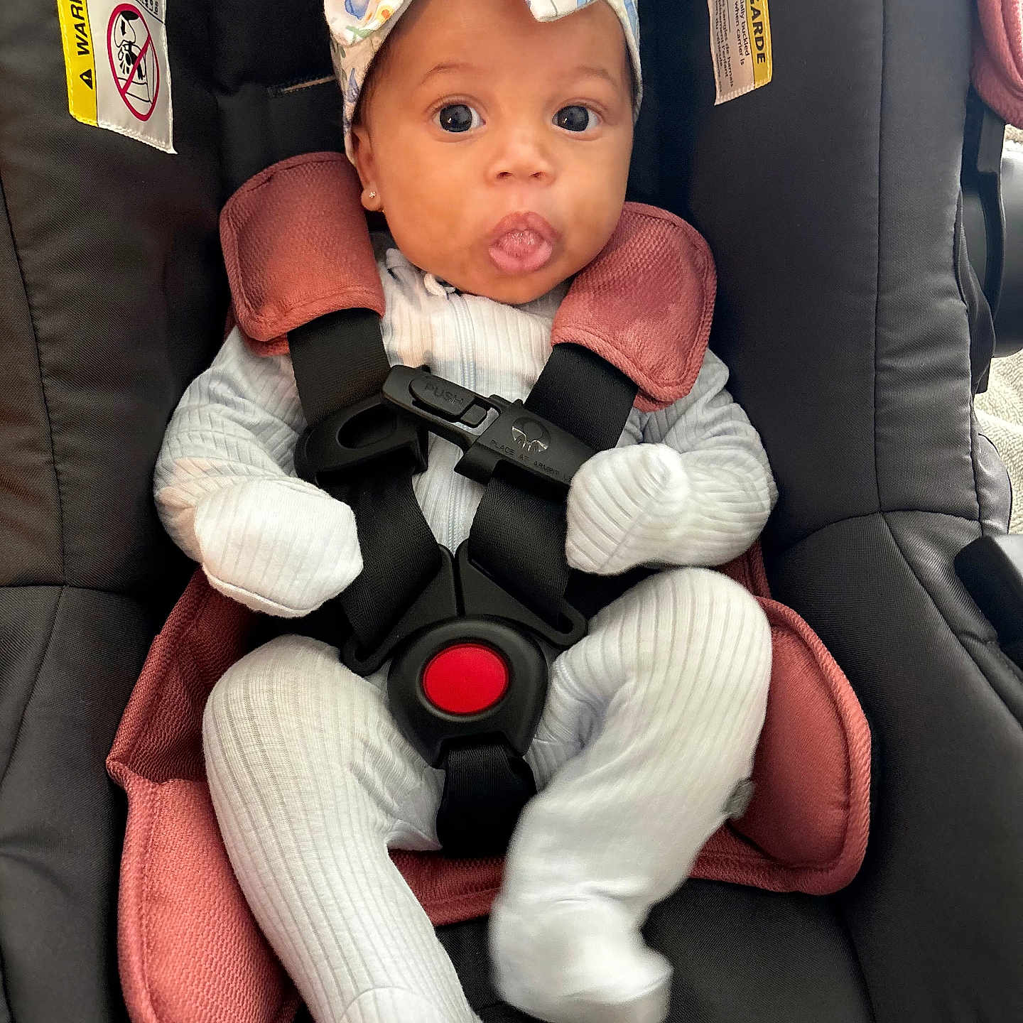 Rayne joined the competition — help win amazing prizes! baby, black_car_seat, bow, car_seat, child, cute, expression, face, headband, indoor, infant, pink_cushion, ribbed_clothing, safety_harness, seat_belt, sitting, small_person, tongue_out, white_outfit, wide_eyes
