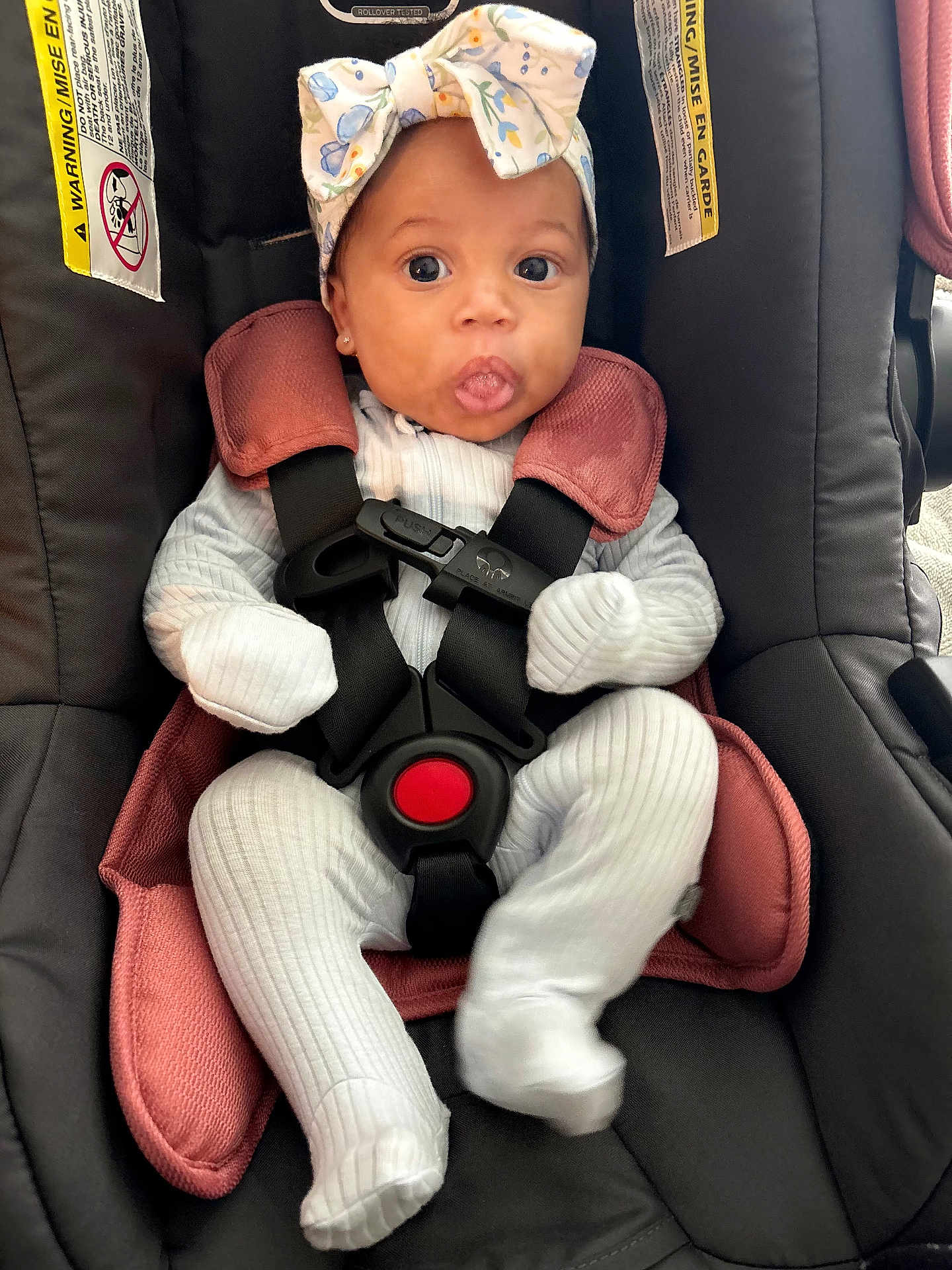 Rayne joined the competition — help win amazing prizes! baby, car_seat, infant, white_outfit, headband, bow, tongue_out, safety_harness, cute, child, seat_belt, pink_cushion, black_car_seat, ribbed_clothing, indoor, small_person, expression, face, wide_eyes, sitting