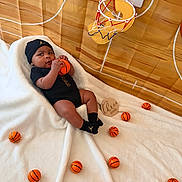 Quincy joined the competition — help win amazing prizes! baby, basketball, miniature_basketball, baby_clothing, black_hat, white_blanket, mini_basketball_hoop, sports_theme, indoor, child, infant, toy, playful, sporty, floor, background, person, cute, sitting, black_outfit