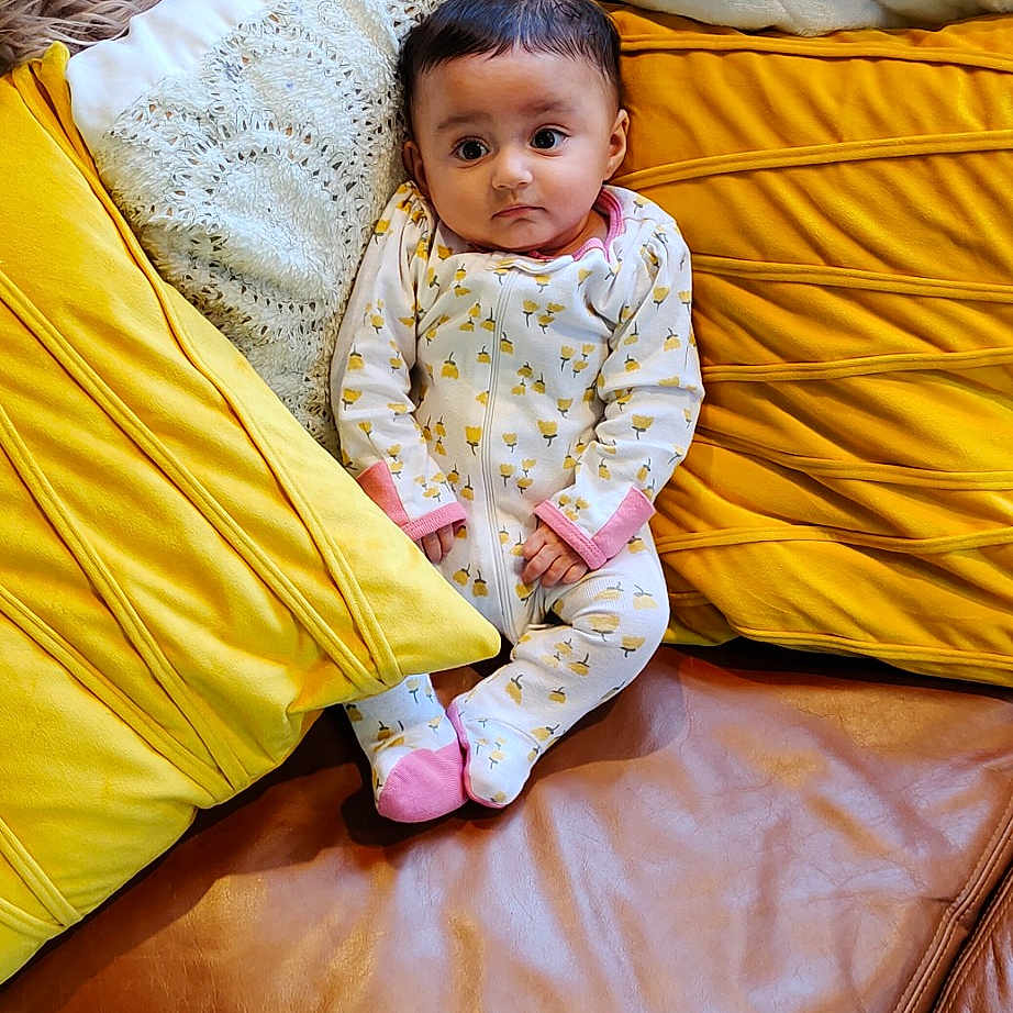 Heer is registered to the contest to win money with this photo: baby, baby_toddler_clothing, bed_sheet, bedding, child, comfort, flooring, fun, grass, happy, leisure, linens, magenta, mammal, outerwear, sitting, textile, throw_pillow, toddler, wood