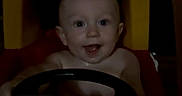 Ledger is registered to the contest to win money with this photo: baby, infant, child, smiling, face, portrait, toy_steering_wheel, toy_car, sitting, indoor, home, playroom, dark_lighting, photograph, smartphone_screen, camera_interface, steering_wheel, happy, looking_at_camera, furniture