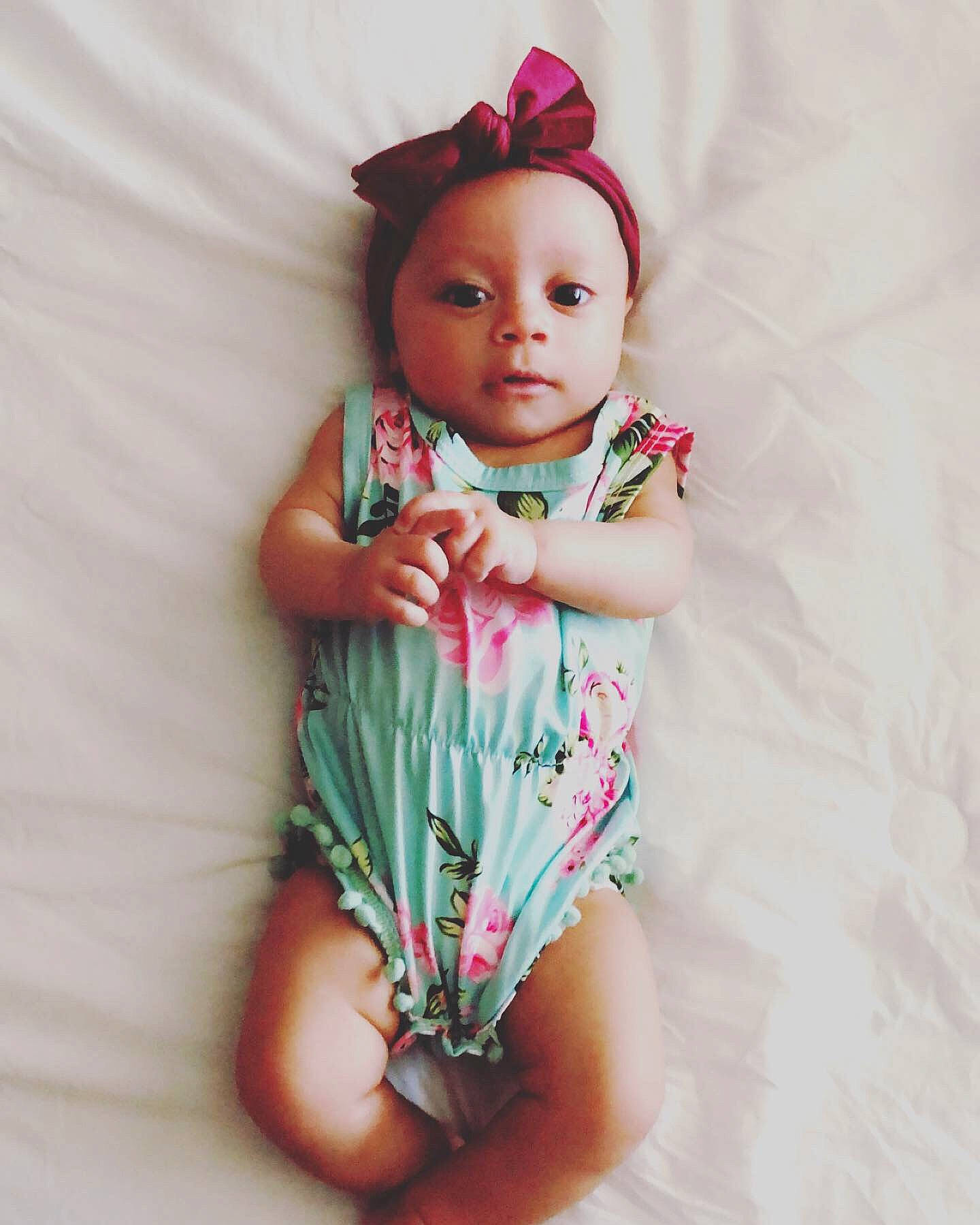 Jemma is registered to the contest to win money with this photo: baby, brown_hair, cheek, child, doll, fashion_accessory, flower, hair_accessory, hand, head, headgear, joint, lip, person, pink, plant, product, skin, smile, toddler