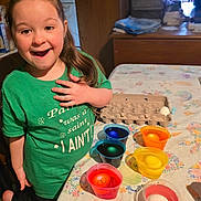 Bizzy is registered to the contest to win money with this photo: child, green_shirt, smiling, table, colorful_cups, eggs, egg_carton, indoor, decorating, happy, long_hair, wooden_furniture, playful, crafts, celebration, festive, person, home, expression, fun