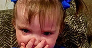 Winnie joined the competition — help win amazing prizes! toddler, child, blue_bow, blue_shirt, strawberry_graphic, hand_covering_mouth, shy, surprised, indoor, couch, patterned_cushion, brown_hair, pigtails, portrait, person, young_child, cute, expression, casual, closeup